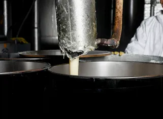 adhesive pouring out of a metal tube into a metal barrel