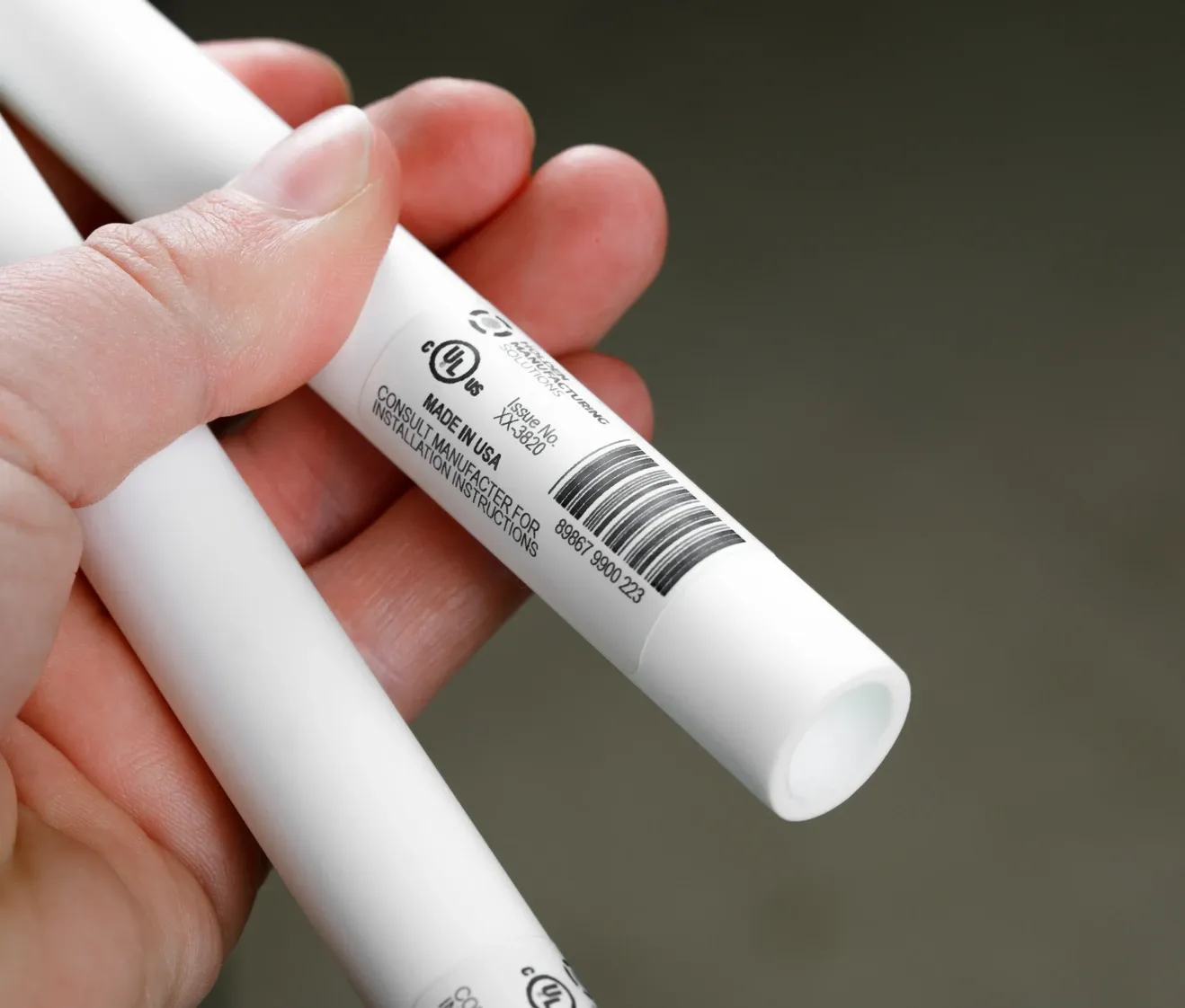 Hand holding two white PVC pipes with barcode labels