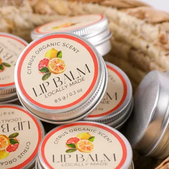 Stack of lip balm tins with decorative floral labels and woven basket
