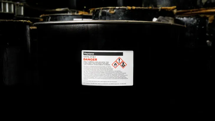 Black chemical drum with white hazmat label displaying safety symbols and warnings