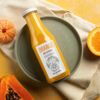 Glass bottle of orange juice with custom label on ceramic plate