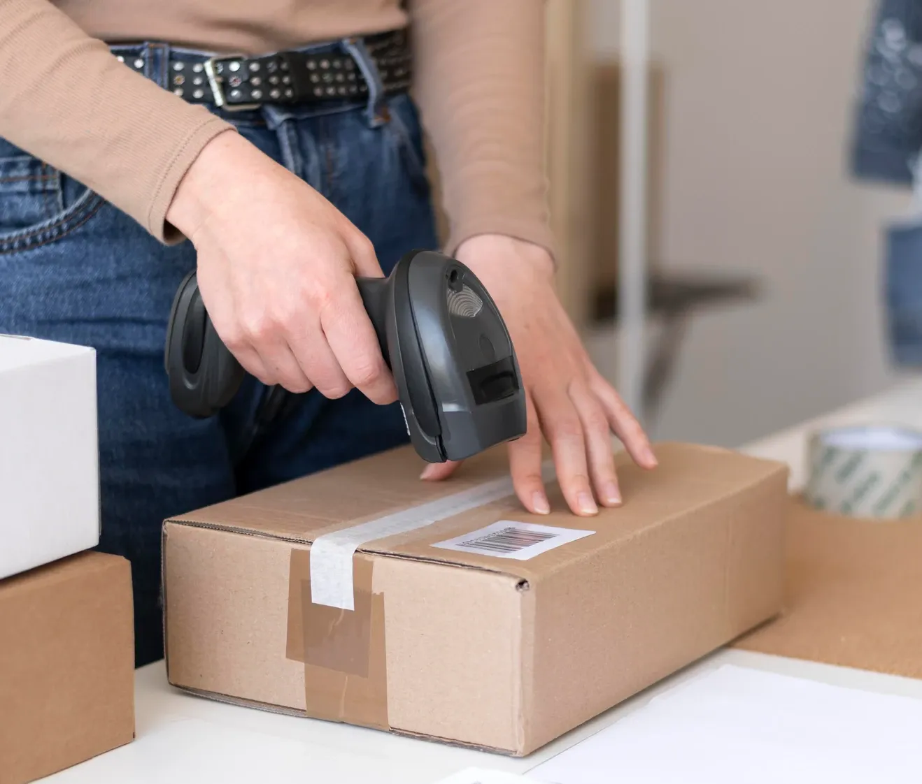 a person using a handheld barcode scanner to scan a barcode label on a rectangular cardboard box