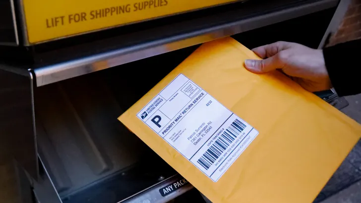 Yellow mailer envelope with thermal shipping label being placed into postal collection box