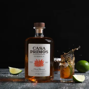 Premium tequila bottle with artisan label displayed on dark background with cocktail glass