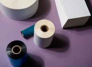 rolls of thermal transfer label materials on purple background with blue and black ribbons