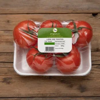 Fresh tomatoes in clear plastic package with product label on rustic wooden surface