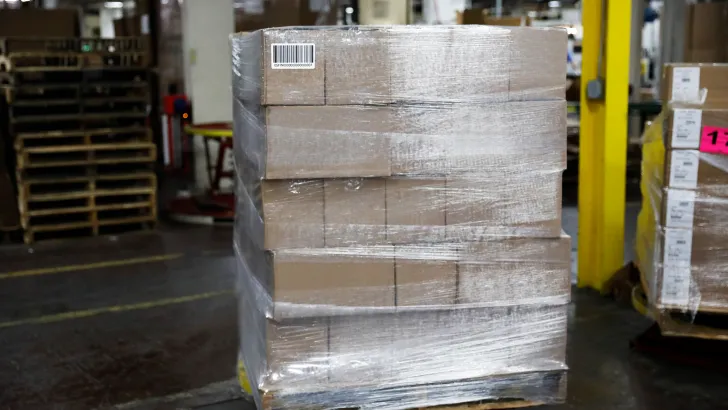 Shrink-wrapped pallet of cardboard boxes in warehouse with forklift