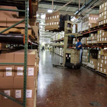 Wide warehouse aisle with forklift operator moving pallets between tall storage racks